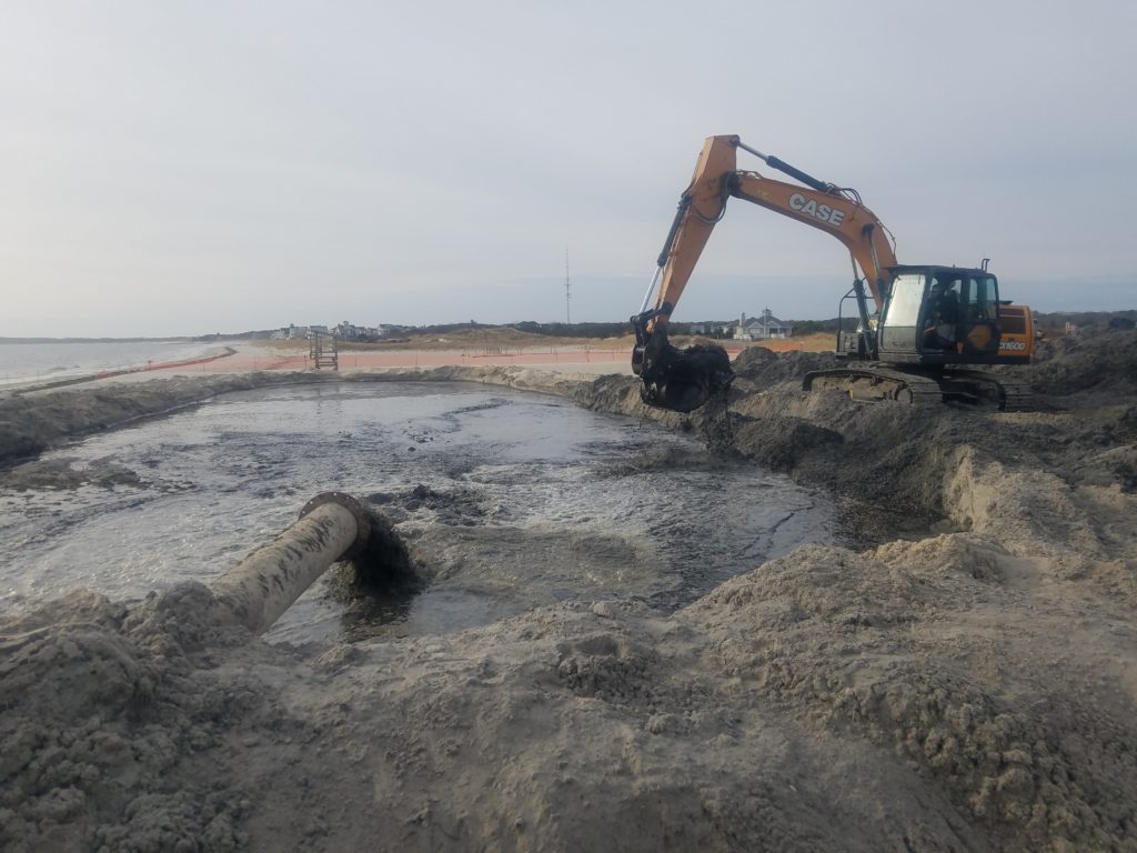 Excavator moving dredged material from the dewatering basin onto the beach