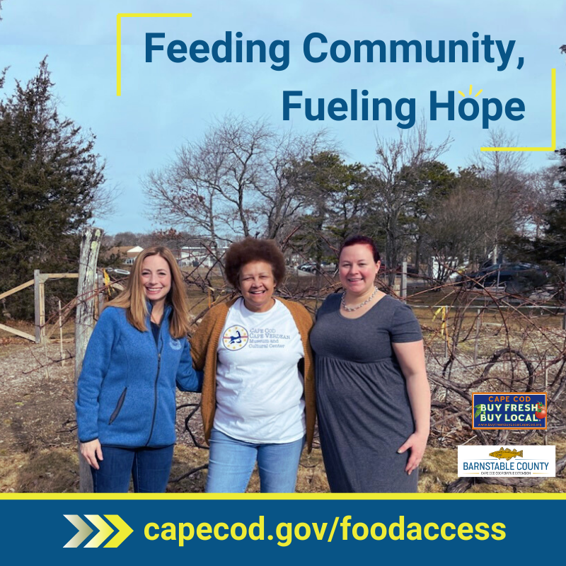 Three smiling women stand together in an outdoor community garden. One woman wears a blue jacket, another wears a white t-shirt with a Cape Verdean Cultural Center logo, and the third wears a gray dress. The text "Feeding Community, Fueling Hope" is displayed above them, with a yellow and blue banner below that reads "capecod.gov/foodaccess." The Cape Cod Buy Fresh Buy Local and Barnstable County logos appear in the bottom right corner.