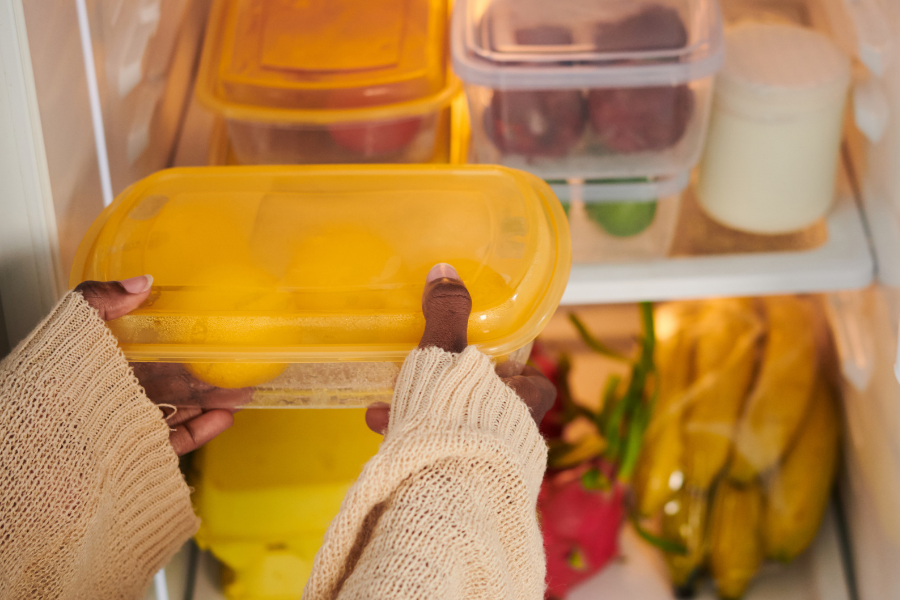 Hands holding a yellow food storage container inside a refrigerator during a power outage, with fresh produce and milk visible on the shelves.