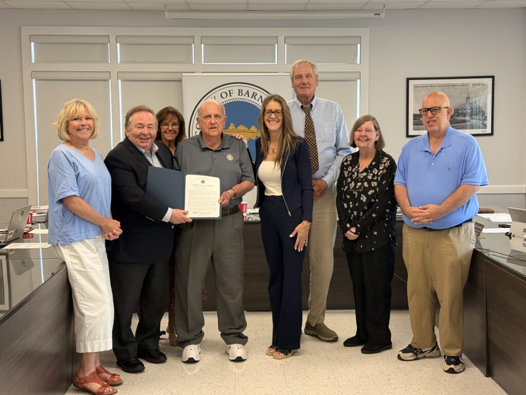 Barnstable County Commissioners honored Bourne Town Clerk Barry Johnson during their June 29, 2026, meeting in Bourne in recognition of his decades of dedicated public service. Pictured (left to right): Barnstable County Commissioner Sheila Lyons; Barnstable County Commissioner and Chair Mark Forest; Bourne Select Board Vice Chair Anne-Marie Siroonian; Bourne Town Clerk Barry Johnson; Bourne Select Board Chair Melissa Ferretti; Barnstable County Commissioner and Vice Chair Ron Bergstrom; Bourne Select Board Clerk Mary Jane Mastrangelo; and Bourne Select Board Member Peter Meier.