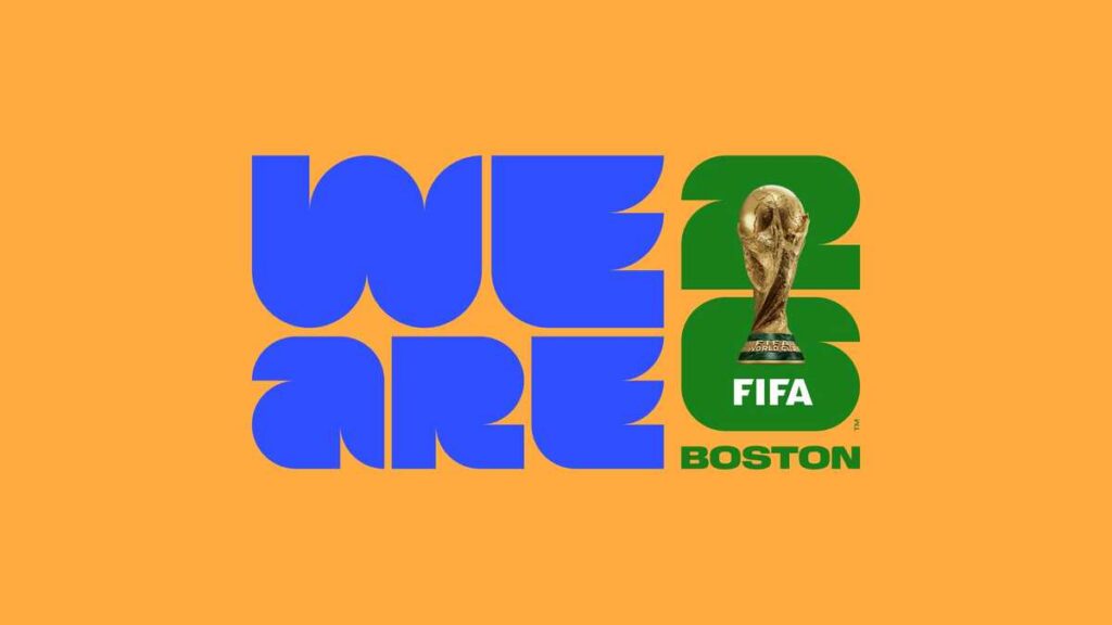 Logo for the FIFA World Cup 2026 Boston host city campaign. The design features large stylized blue letters spelling “WE ARE” on the left and green numbers “26” on the right, with the FIFA World Cup trophy integrated into the numeral 2. Below the trophy is the word “FIFA” in white, and “BOSTON” appears in green at the bottom. The logo is set against a solid orange background.