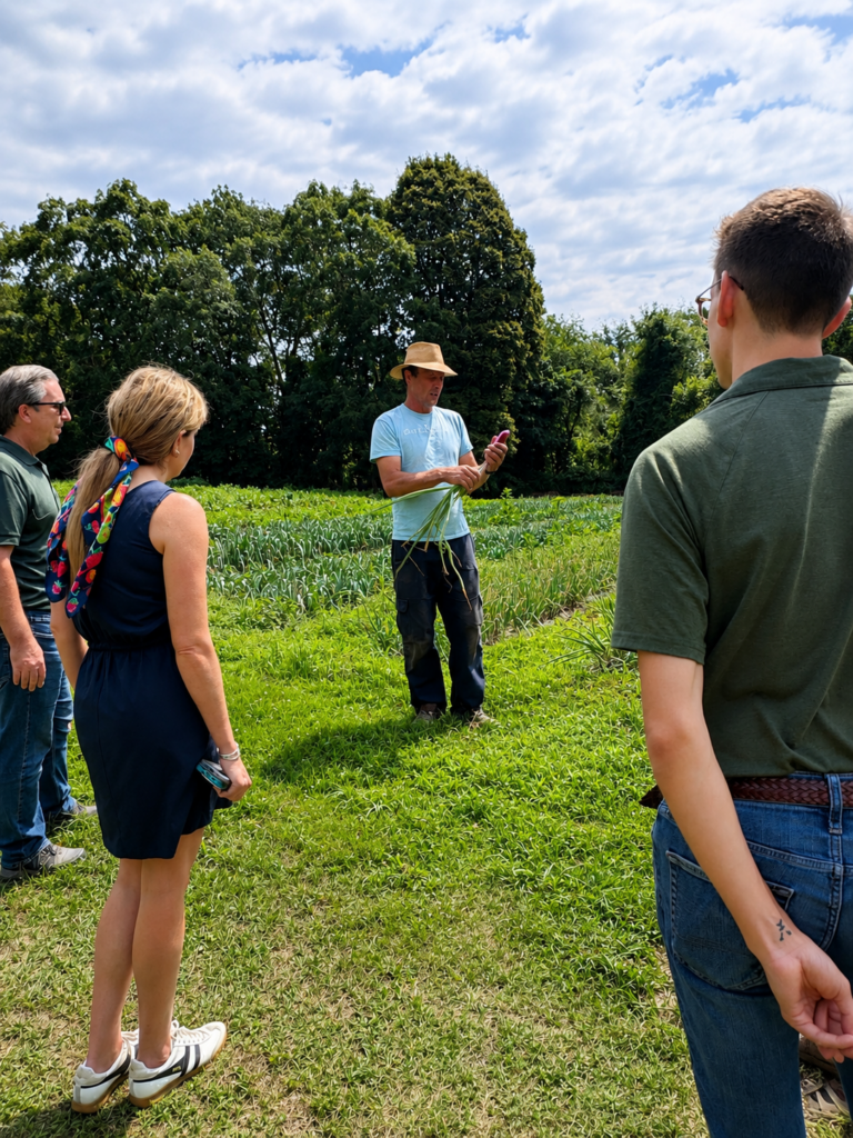 Bay End Farm owner Kofi Ingersoll stands in an onion field demonstrating onion production and discussing crop management with visiting Massachusetts Department of Agricultural Resources (MDAR) staff during a farm tour.
